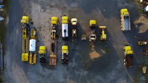 Overhead view of yellow construction trucks parked in neat rows on a gravel surface.
